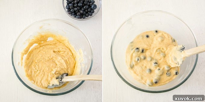 A spatula gently folding fresh blueberries into a glass bowl of muffin batter