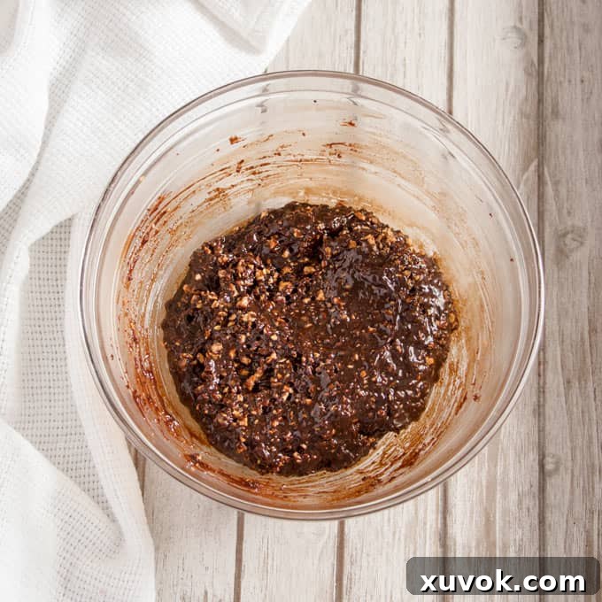 A close-up shot of a bowl filled with rich hazelnut praline ganache, showcasing its thick, creamy texture dotted with praline crumbs.