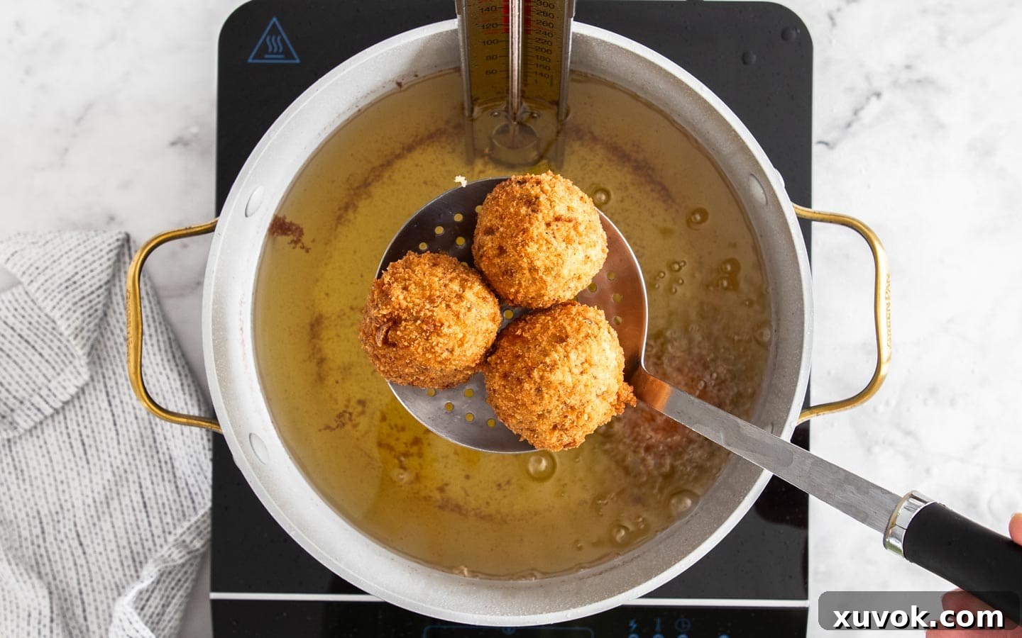 Slotted spoon scooping 3 golden-brown chorizo arancini from hot oil.
