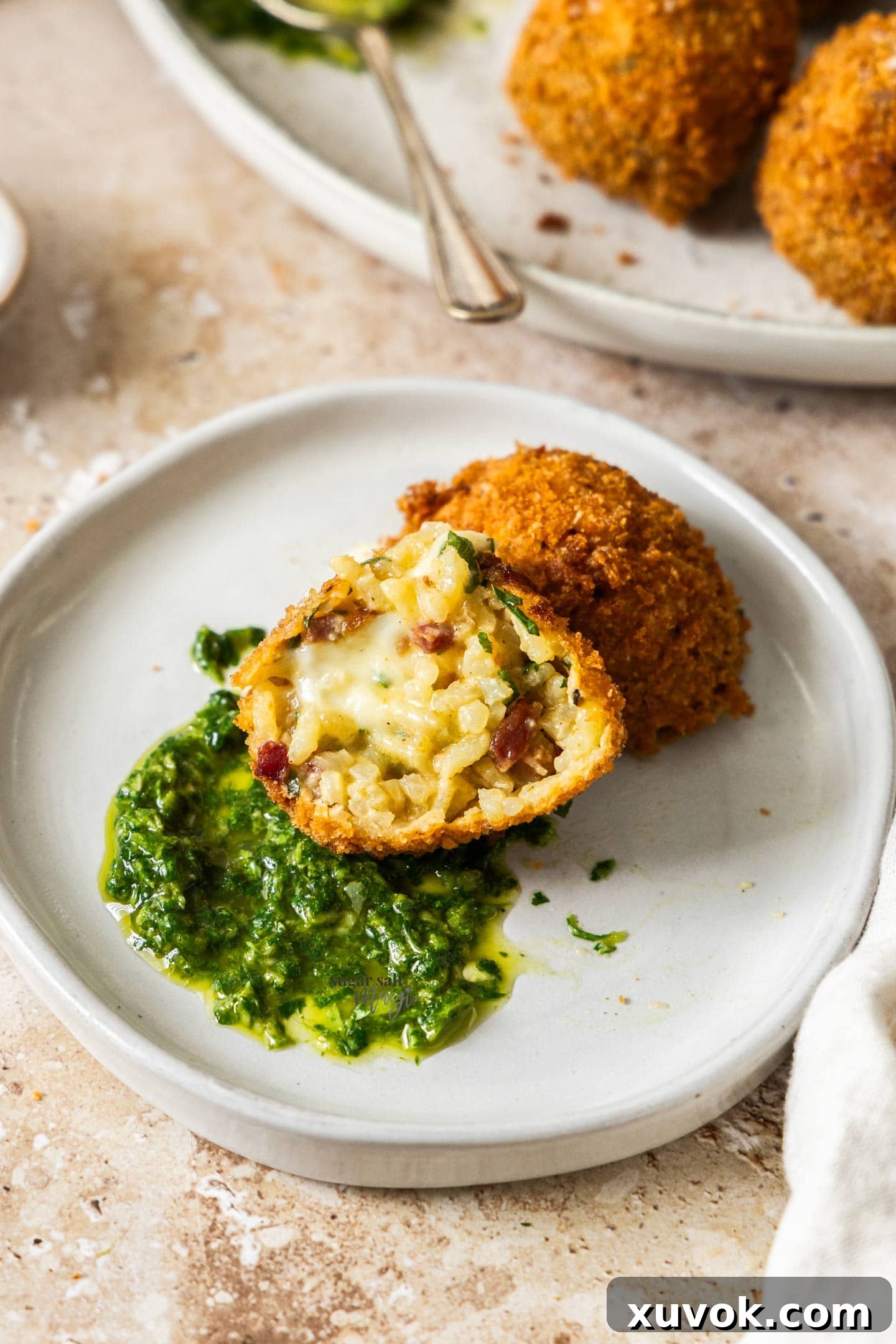 A chorizo arancini broken in half sitting on green sauce.