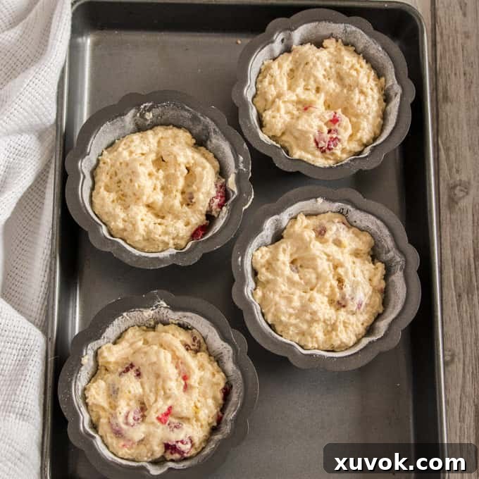 Adding batter into greased mini bundt tins before baking.