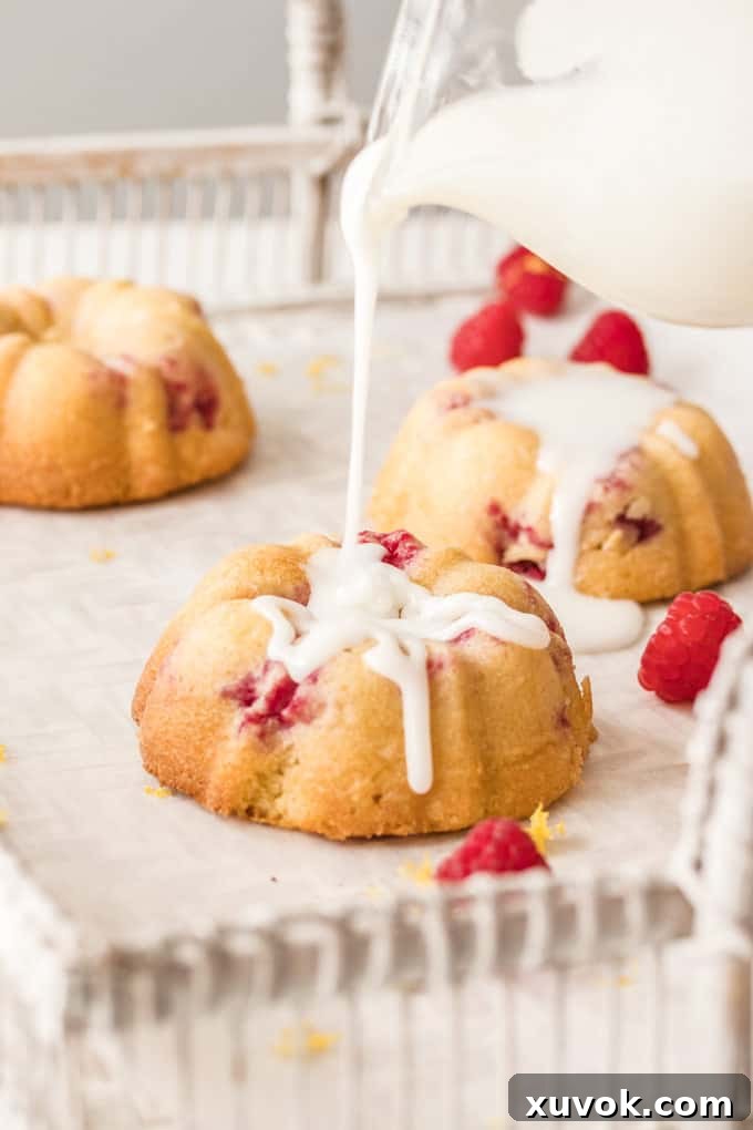Lemon Icing drizzling beautifully over a mini bundt cake, with fresh raspberries strewn about for garnish.