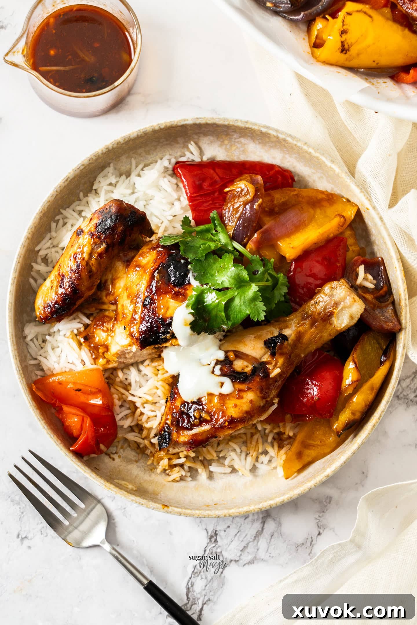 A dish of carved harissa chicken and roasted vegetables served with rice and a dollop of Greek yogurt.