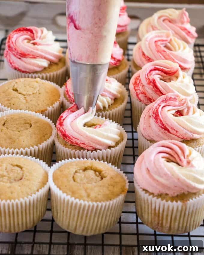 A hand piping the three-tone frosting onto a Peach Melba Cupcake, showing the beautiful swirl of colors.
