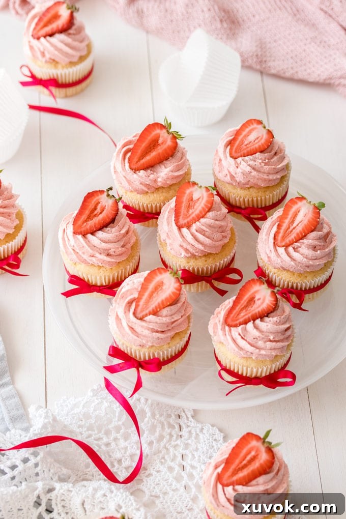 Top down view of a plate of 7 vanilla cupcakes with strawberry buttercream, garnished with fresh strawberries