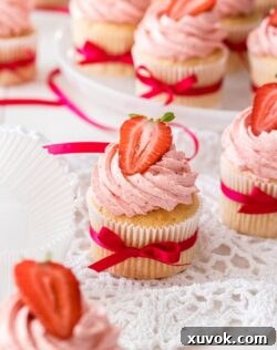 Six Vanilla cupcakes with strawberry buttercream with strawberries on top, on a white plate.