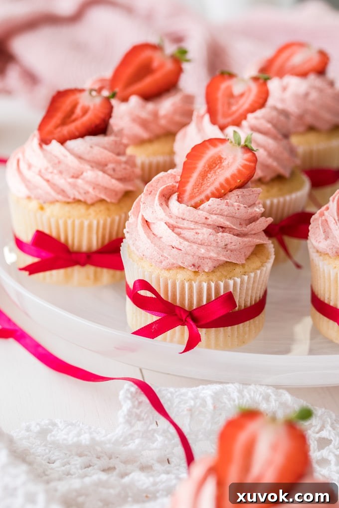 A beautifully arranged plate of vanilla cupcakes topped with strawberry buttercream and fresh strawberry slices.