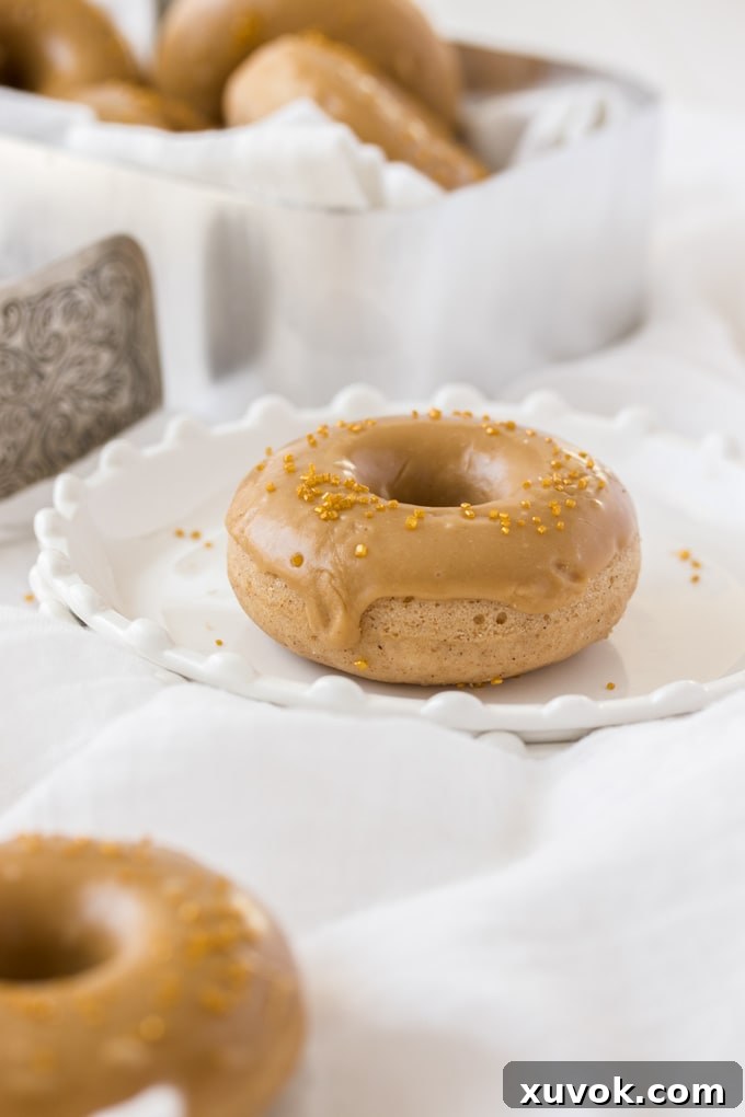 A single cake donut on a small plate, featuring a caramel brown butter icing and a dusting of cinnamon.