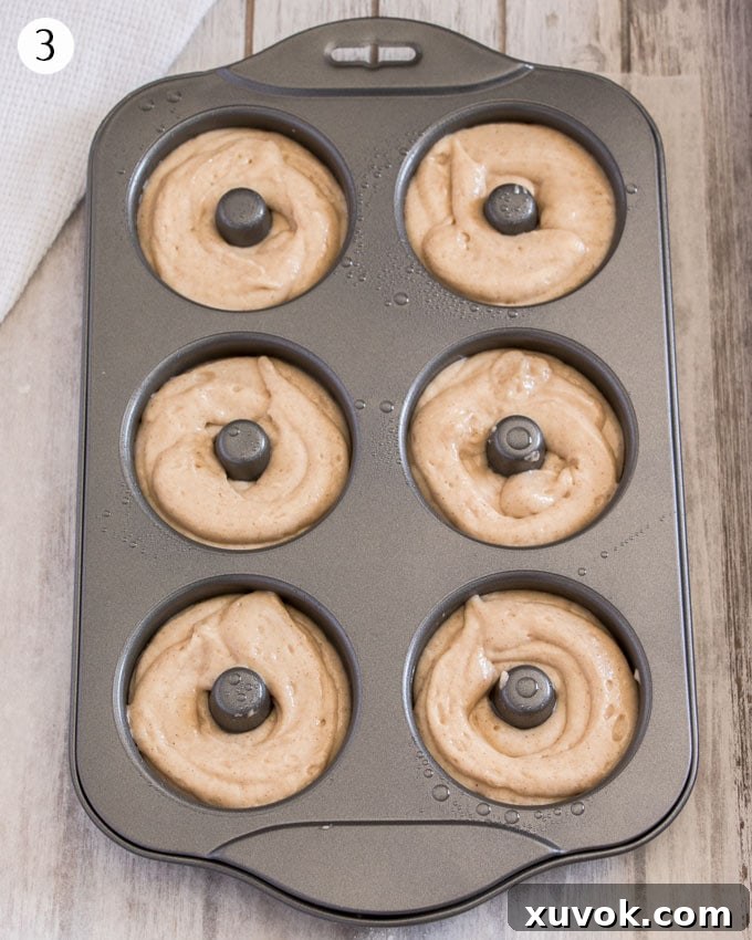 Cake donut batter being piped into a greased donut pan, ready for baking.