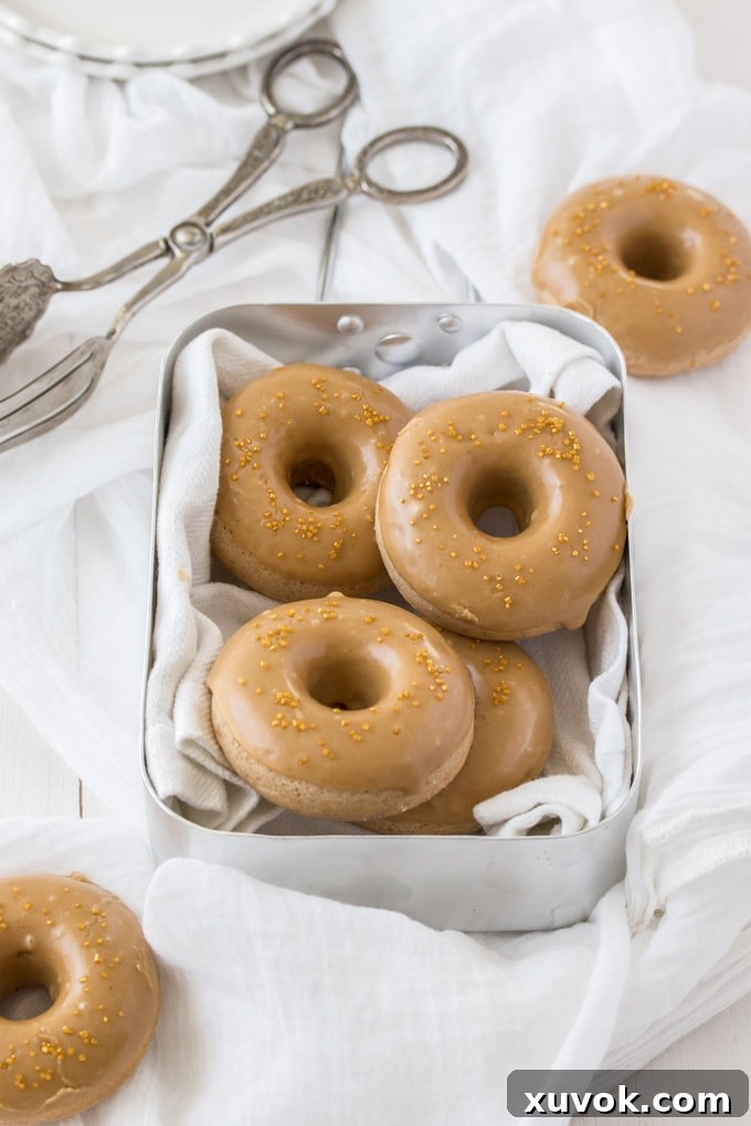 Four cinnamon baked cake donuts in a tin, with two additional donuts on the side, ready to be served.