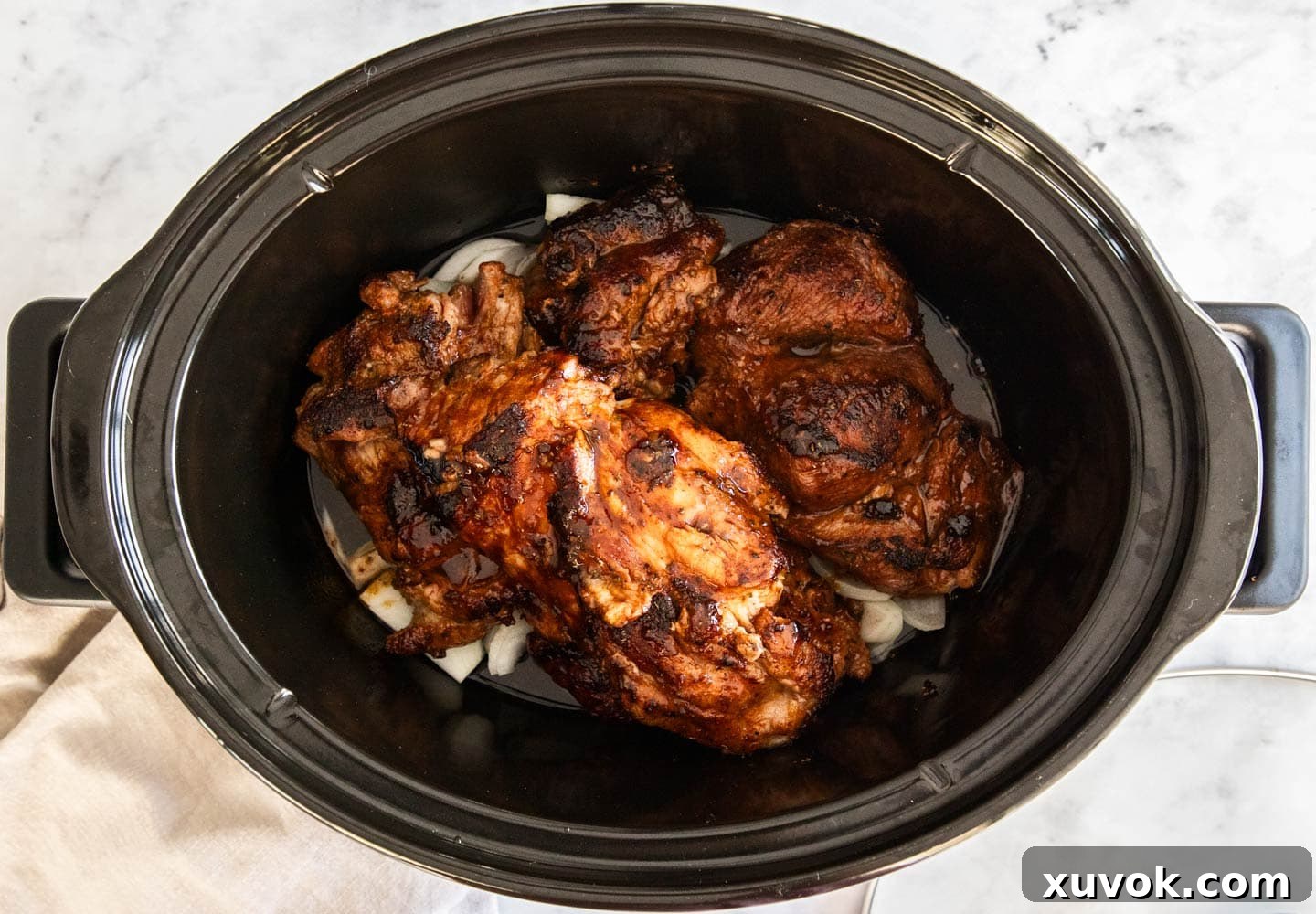The pork in the bowl of a slow cooker on top of onions.