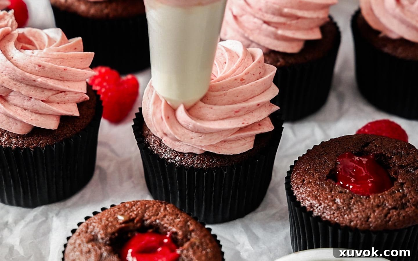 Piping raspberry buttercream onto a chocolate cupcake.