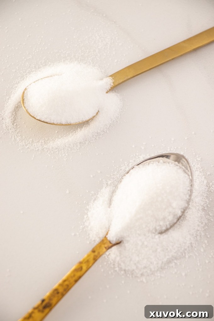 Close-up comparison of two types of granulated sugar on spoons: Caster Sugar and Granulated Sugar, highlighting their different crystal sizes.
