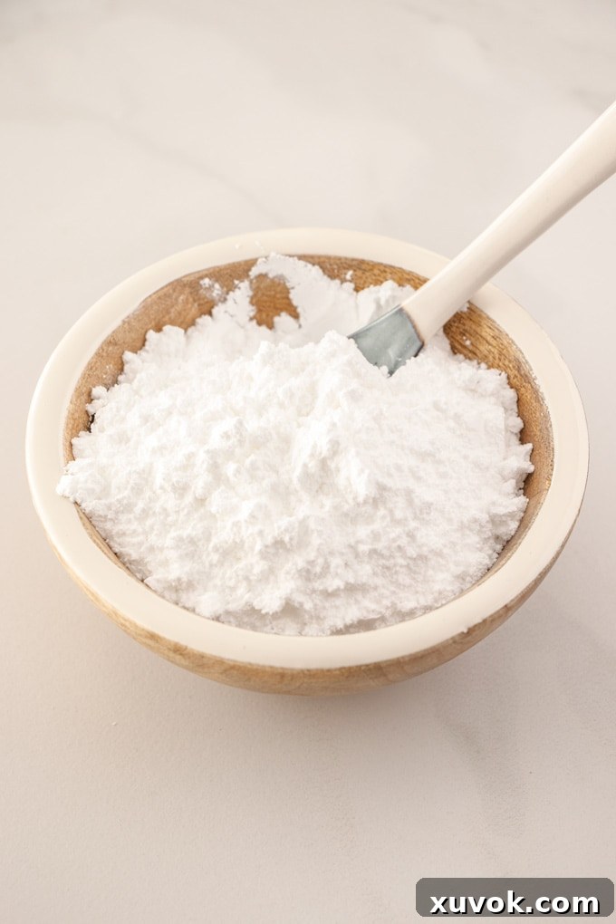 A wooden bowl filled with white icing sugar, with a spoon sticking out, set against a clean background.