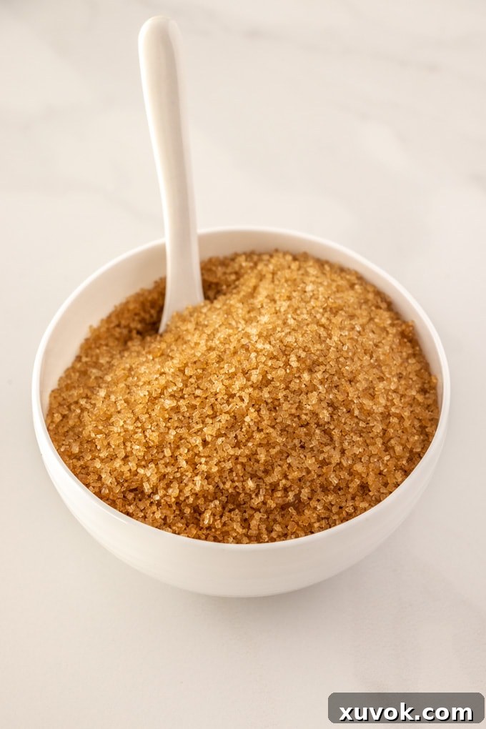 A wooden bowl filled with demerara sugar, featuring large golden-brown crystals, with a spoon resting inside.