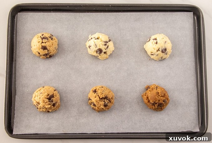 Six mounds of chocolate chip cookie dough arranged on a baking tray, each representing a different sugar type used in the recipe.