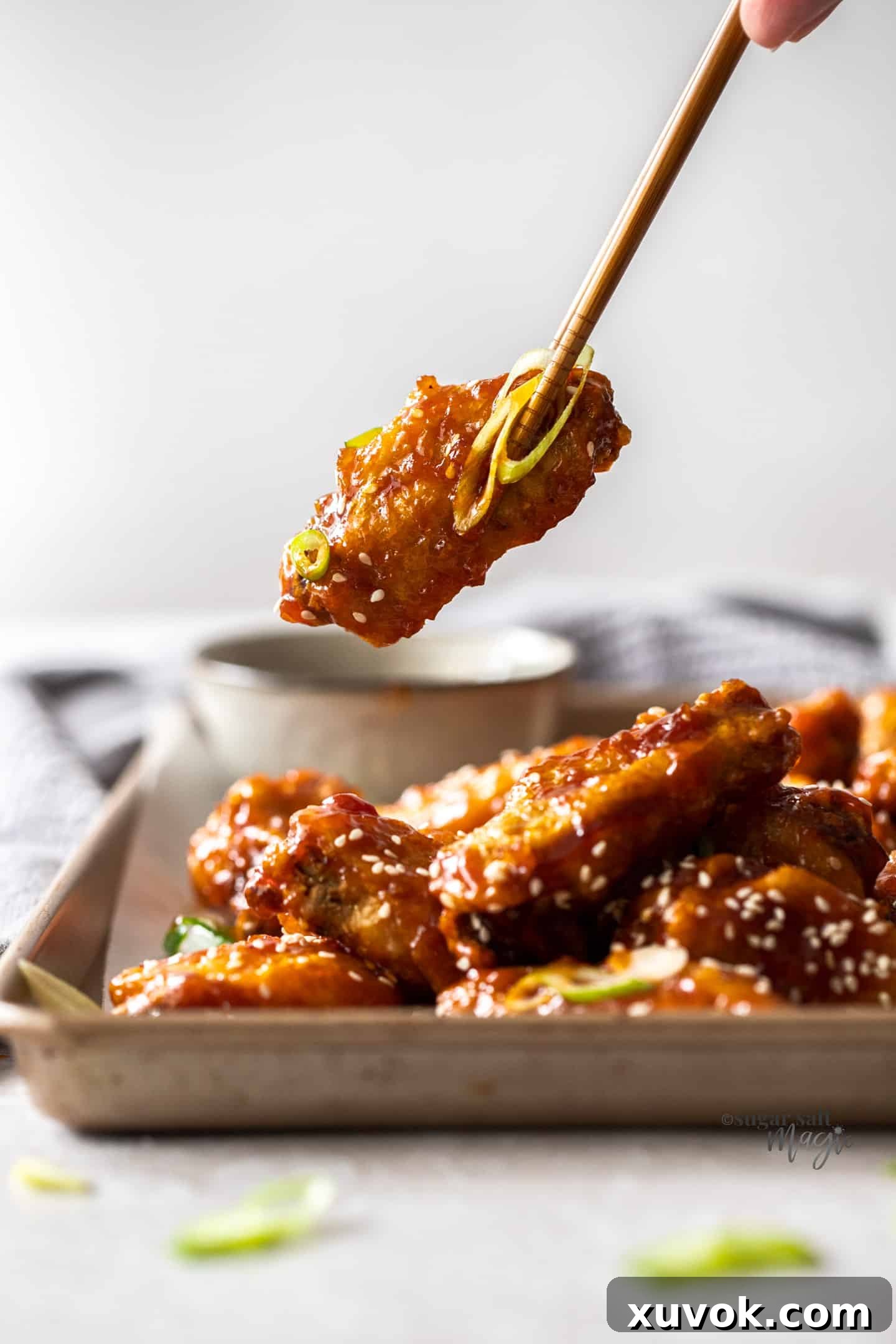 A fried chicken wing being held by a pair of chopsticks, highlighting its crispy texture and glaze.