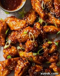 A closeup of a pile of fried sticky chicken wings on a baking tray, garnished with sesame seeds.