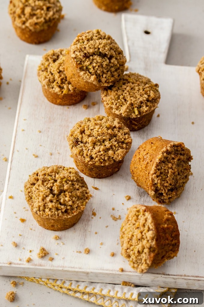 Eight perfectly baked carrot cake muffins arranged on a white board, surrounded by golden streusel crumbs.