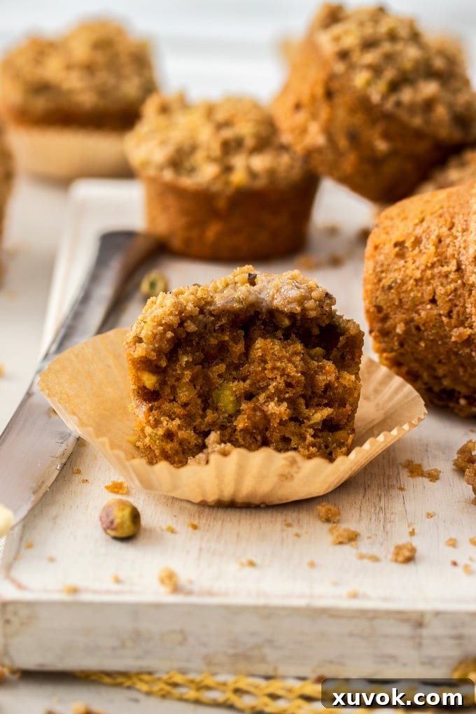 A close-up shot of the inside of a moist carrot cake muffin, revealing finely grated carrots and nuts, with a knife resting beside it on a white board.