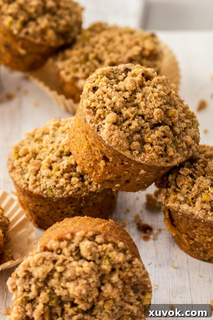 A stack of golden-brown carrot cake muffins with streusel topping on a white cutting board, showing their moist texture.