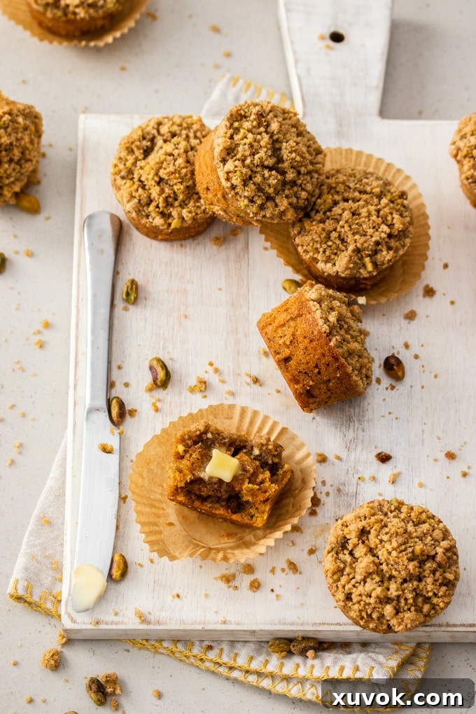 A bird's eye view of six carrot cake muffins, one broken open with butter, on a white board with a knife.