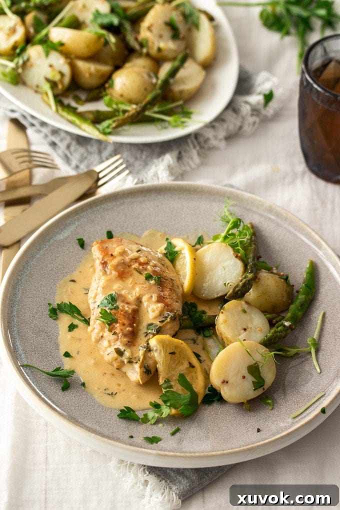 A grey plate with a chicken breast, roasted potatoes, and a rich cream sauce, garnished with fresh thyme.
