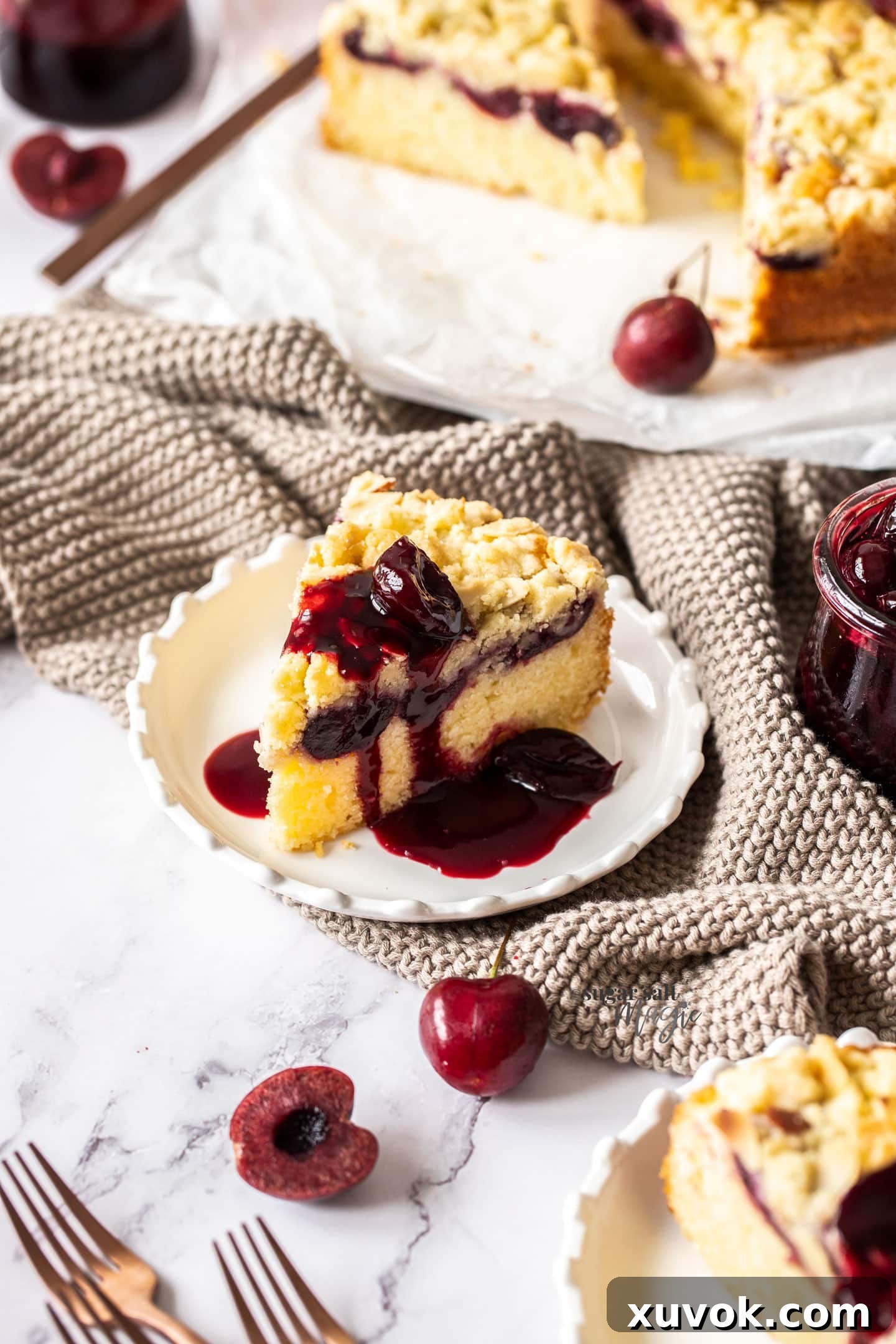 A perfectly baked slice of almond cherry crumb cake on a white plate, glistening with cherry syrup.