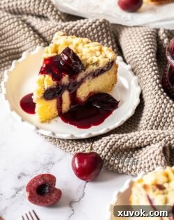 A slice of almond cherry crumb cake on a white plate with cherry syrup drizzled over it