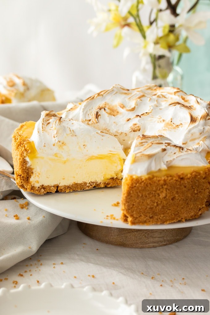 A vibrant lemon meringue cheesecake, meticulously cut to reveal its distinct layers of golden biscuit crust, creamy lemon filling, and fluffy white meringue topping.