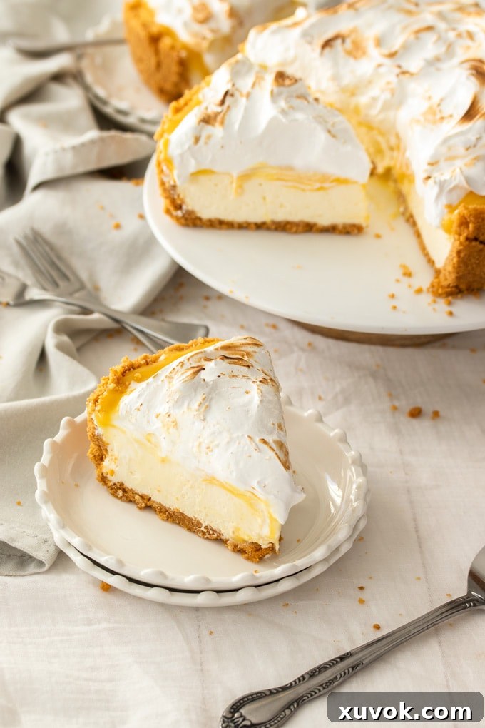 A pristine slice of lemon meringue cheesecake positioned on a white dessert plate, with the magnificent whole cheesecake artfully blurred in the background, highlighting the perfect layers and toasted meringue.