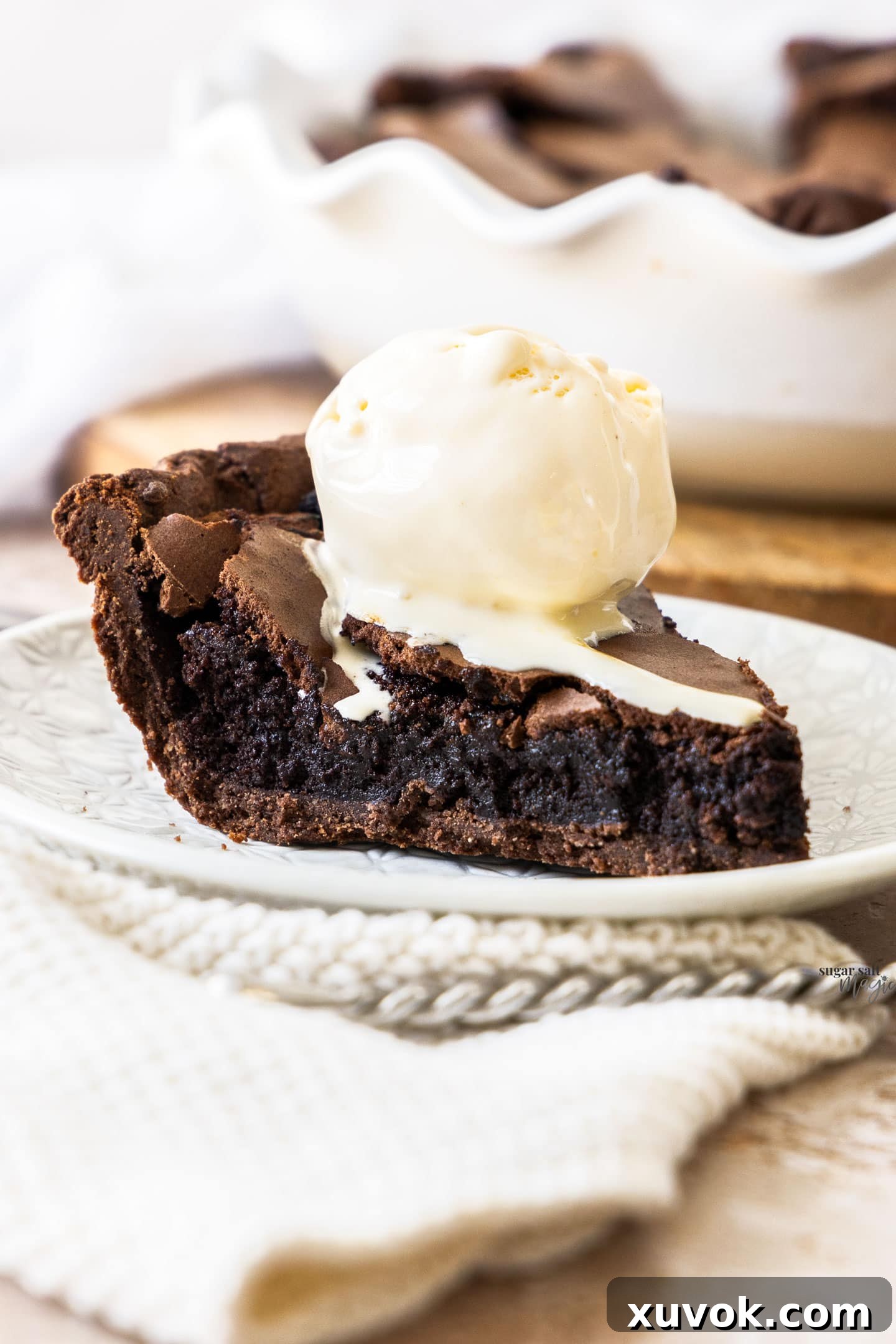 A perfectly sliced piece of Chocolate Brownie Pie, revealing its rich fudgy interior and a delightful crackly top, served on a dessert plate alongside a scoop of creamy vanilla ice cream.