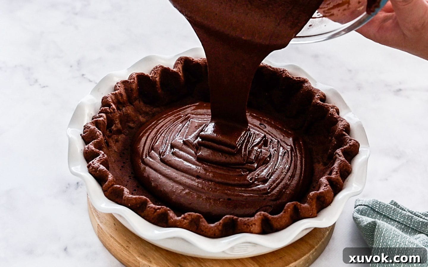 The rich brownie batter being smoothly poured into the par-baked chocolate pie shell, ready for its final bake.
