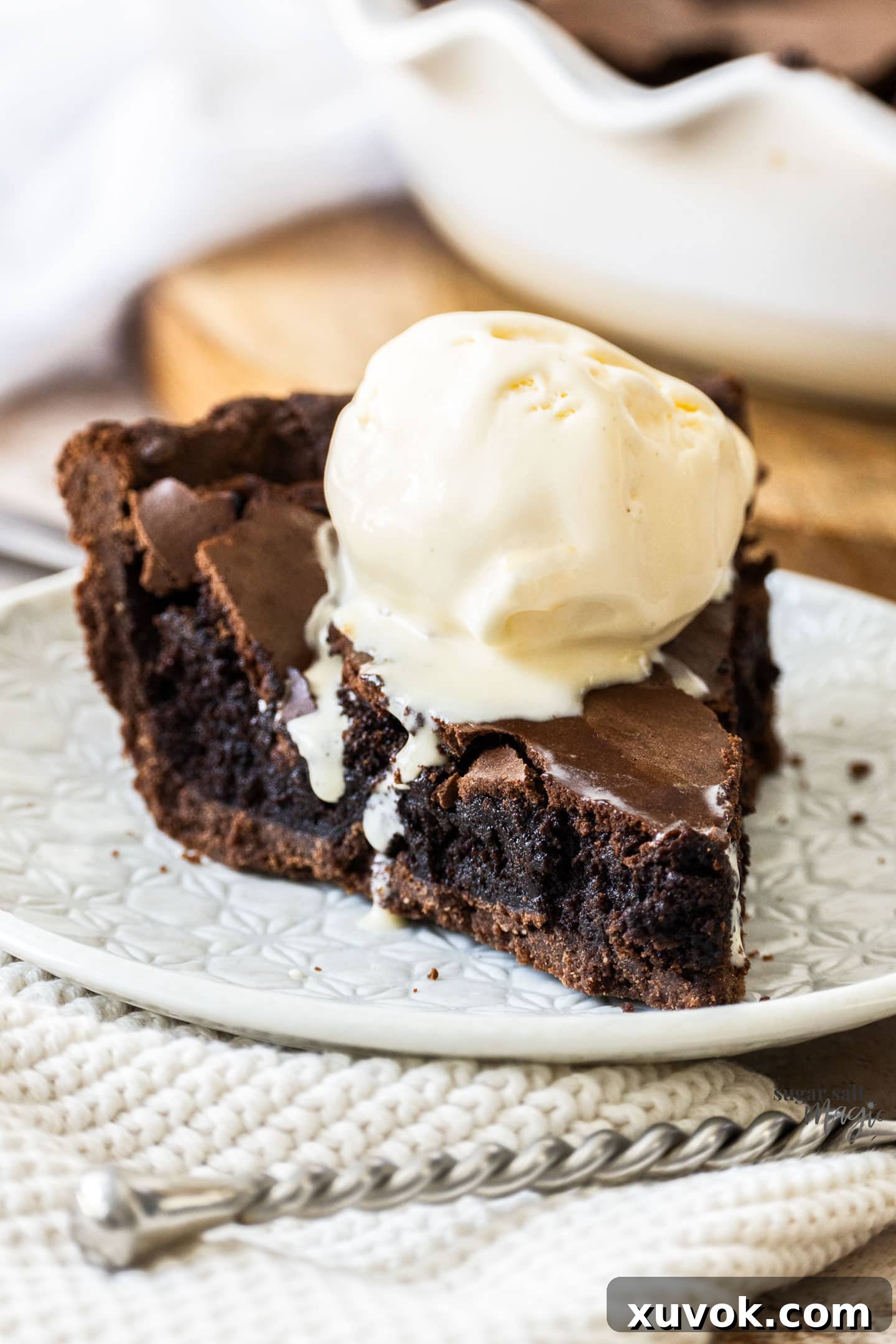 A close-up shot of a single slice of Chocolate Brownie Pie, topped with a melting scoop of vanilla ice cream, highlighting the fudgy texture and crackly crust.