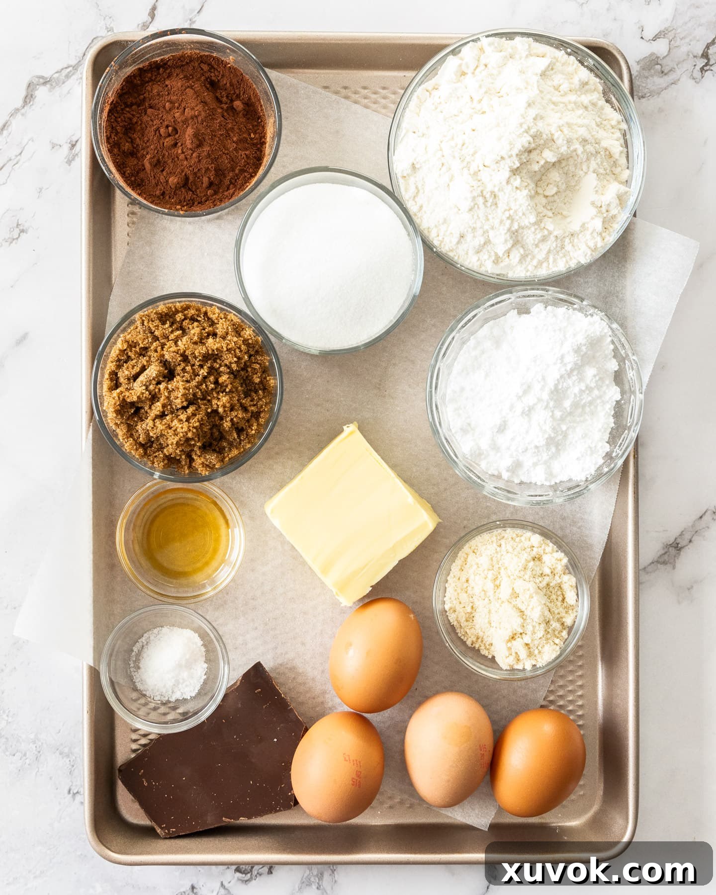 A collection of ingredients laid out, including flour, sugars, cocoa powder, butter, eggs, and dark chocolate, ready for making the brownie pie.