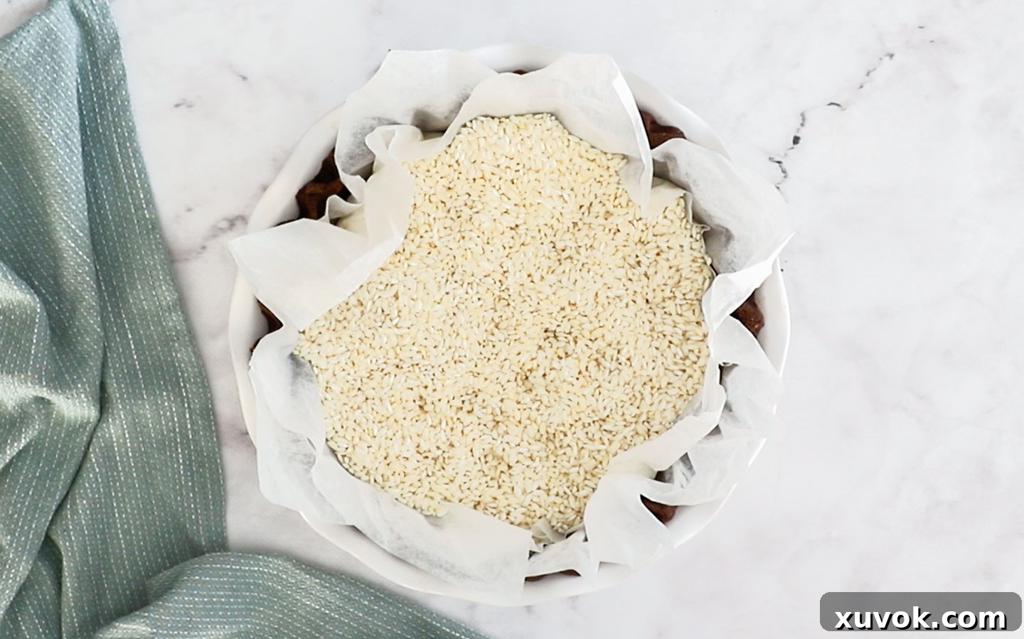 The chocolate pie crust lined with baking paper and filled with pie weights (rice), prepared for blind baking.