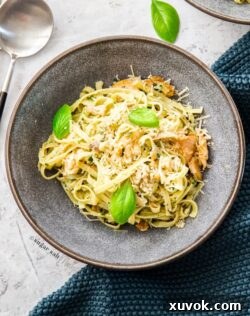 A grey bowl filled with pasta. A green crochet cloth in front and a fork and spoon behind.