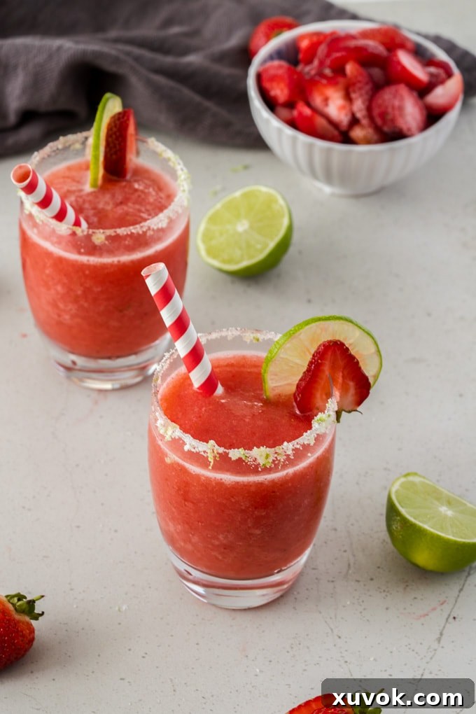 Two glasses filled with frozen strawberry daiquiri with a couple of lime wedges