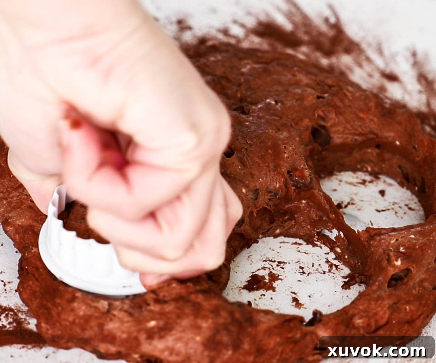 A round cookie cutter pressing into chocolate scone dough to create individual scones.