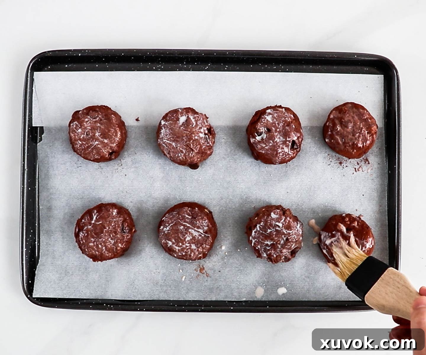 Eight chocolate scones arranged on a baking tray, lightly brushed with milk before going into the oven.