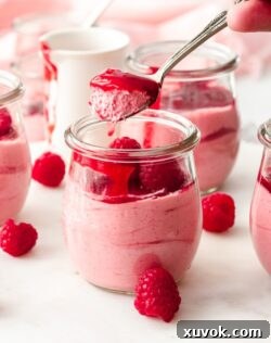A spoon holding pink raspberry mousse just coming out of the glass
