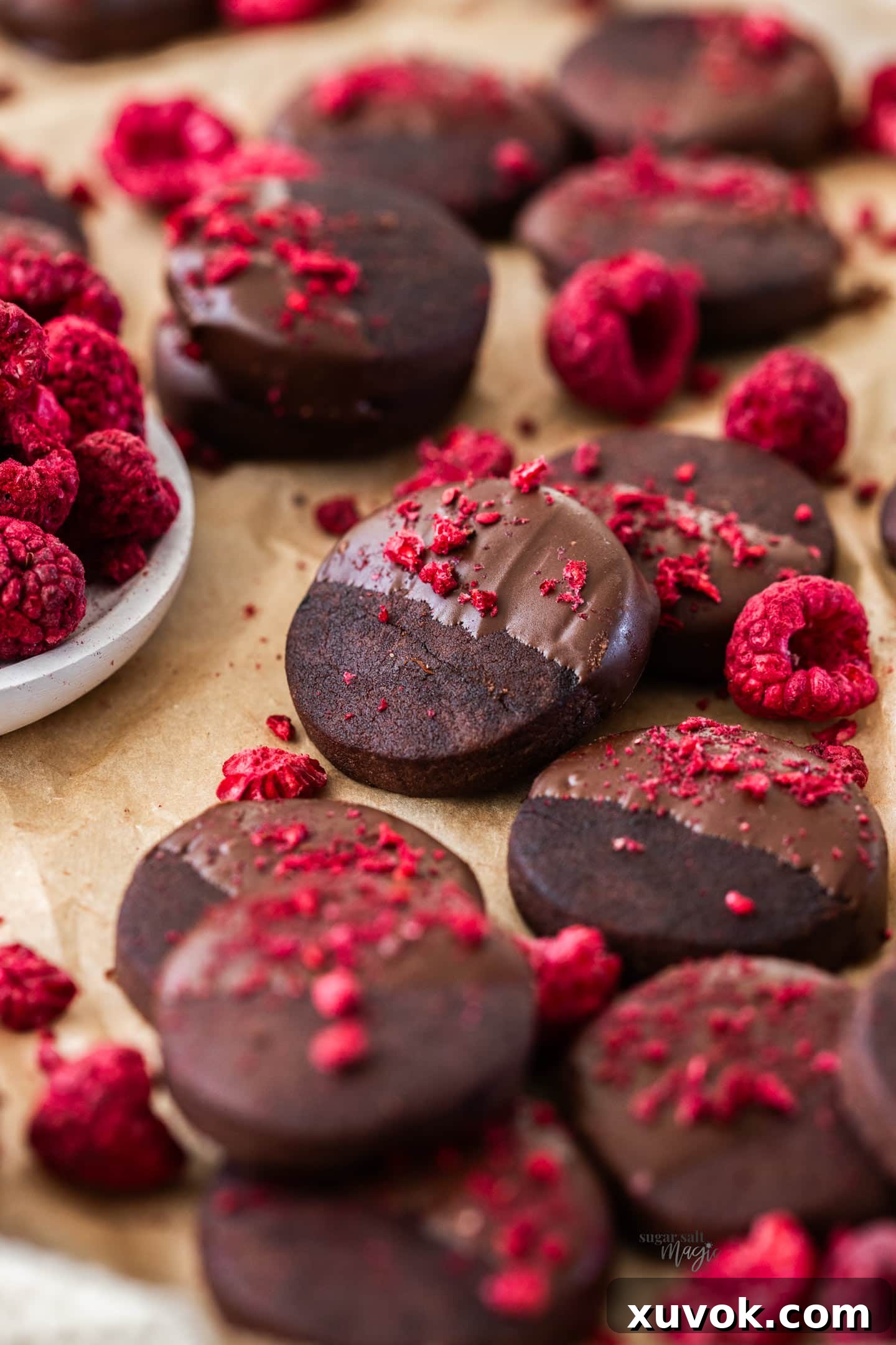 A beautifully arranged batch of chocolate shortbread cookies, artfully scattered with bright freeze-dried raspberries, creating a vibrant contrast.
