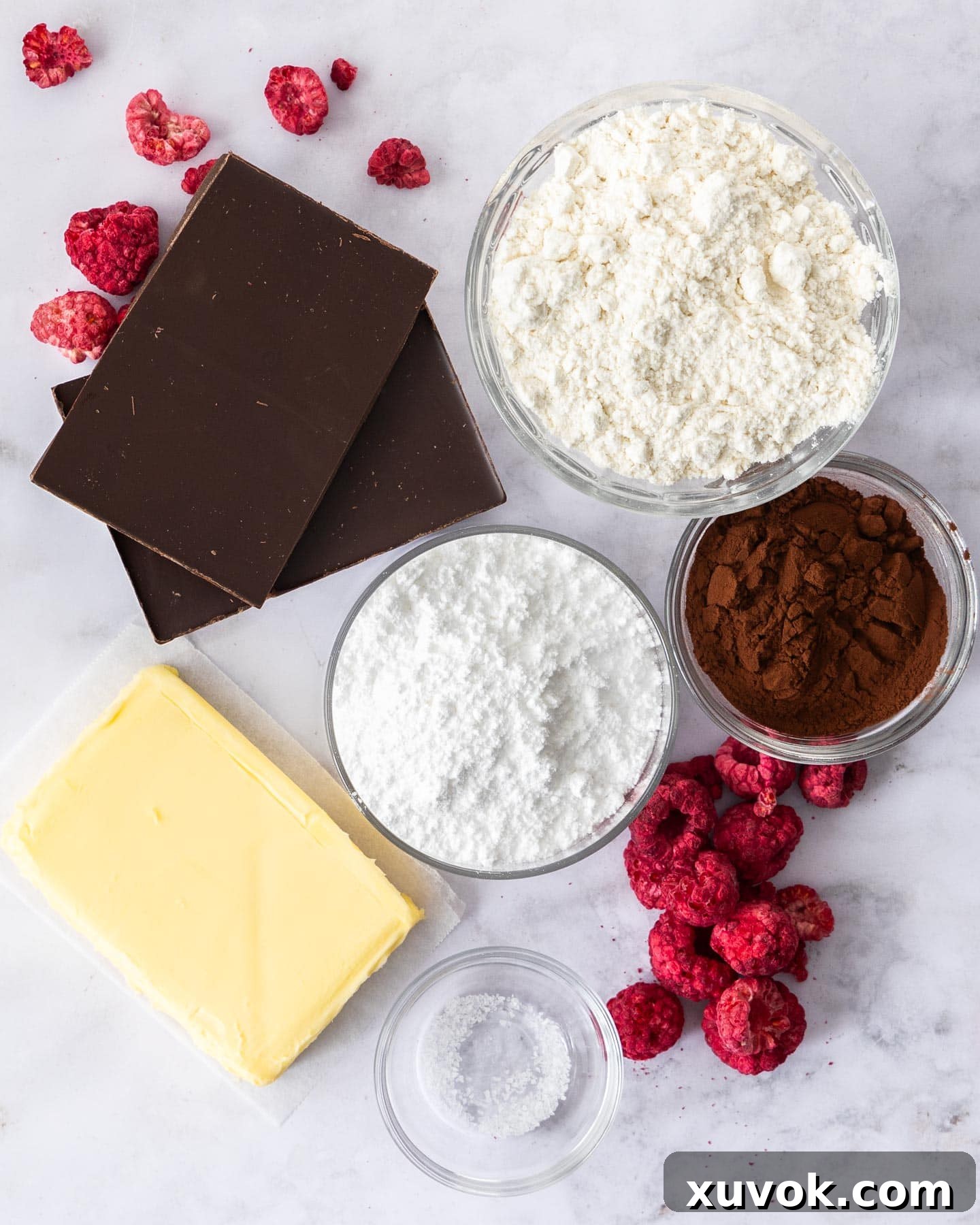 Carefully laid out ingredients for chocolate shortbread, including butter, flour, cocoa, and icing sugar, on a pristine marble surface, ready for baking.