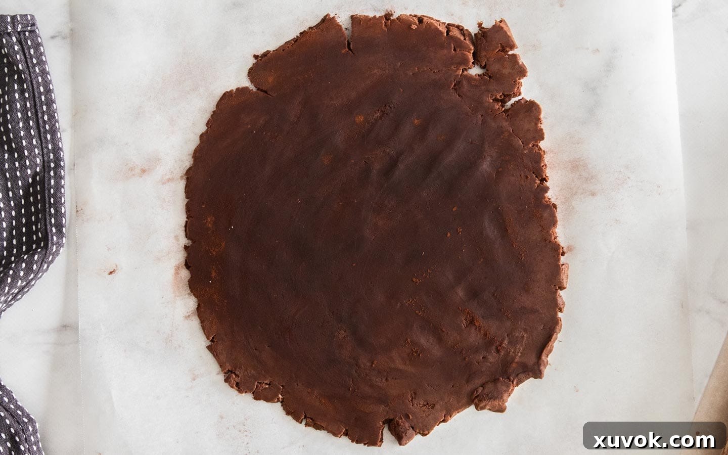 The chocolate shortbread dough expertly rolled out between two sheets of parchment paper, achieving a uniform thickness.
