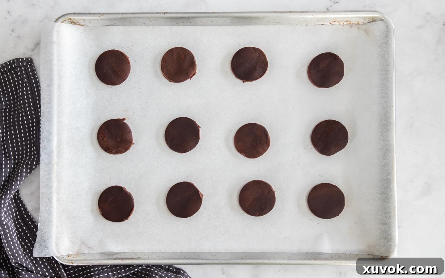 Neatly arranged circles of chocolate cookie dough awaiting their turn in the oven on a parchment-lined baking sheet.