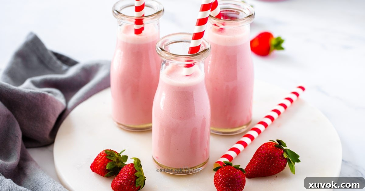 Three bottles of homemade strawberry milk on a marble platter, showcasing a recipe made with real frozen fruit