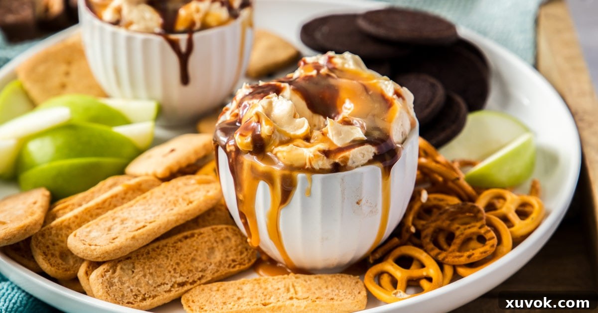 A large white bowl brimming with Snickers Dip, exquisitely layered with chocolate and caramel drizzles down its sides. The dip is surrounded by a tempting array of chocolate cookies and crunchy pretzels, highlighting its rich and indulgent nature.