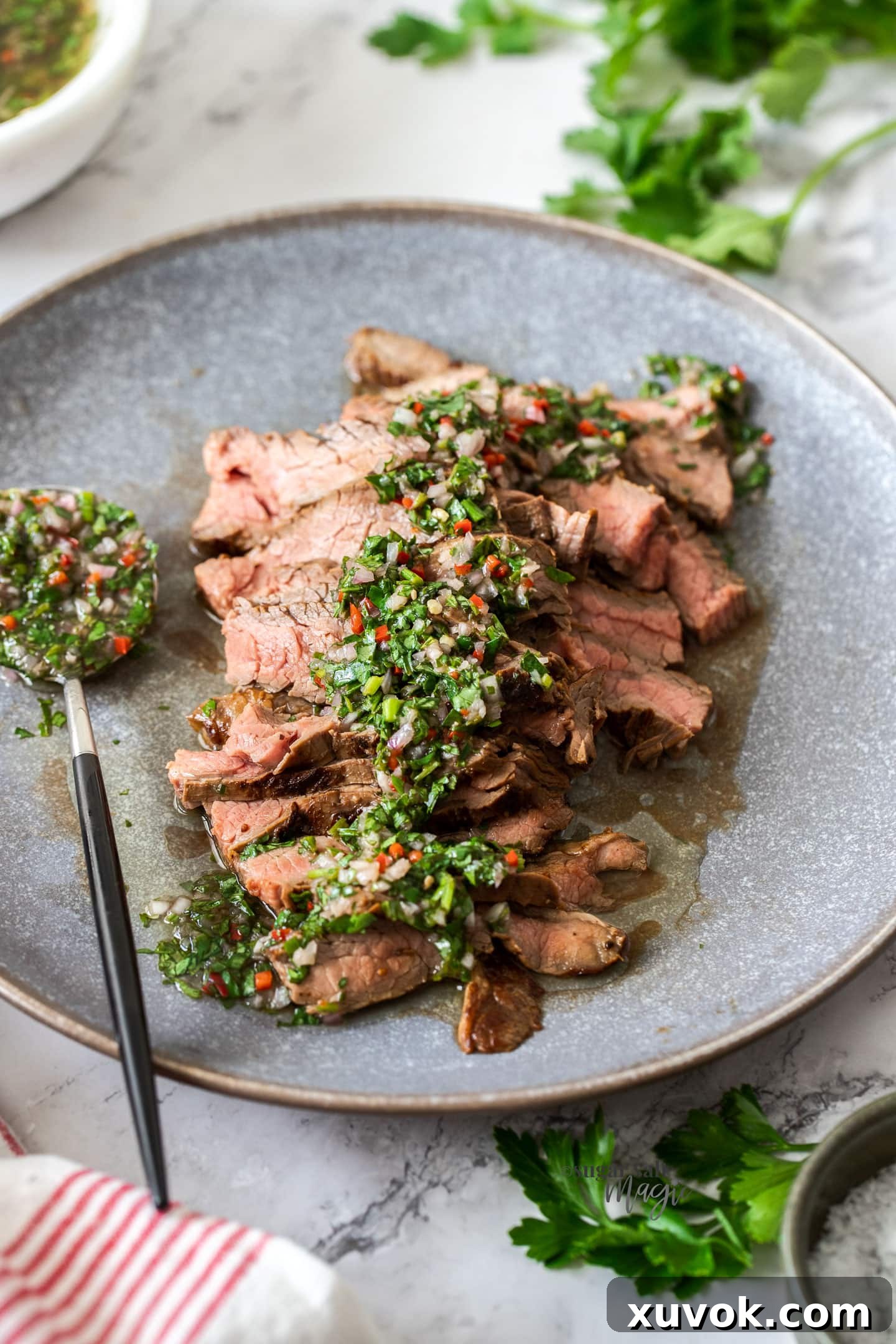 Sliced steak on a grey plate with green sauce over it.