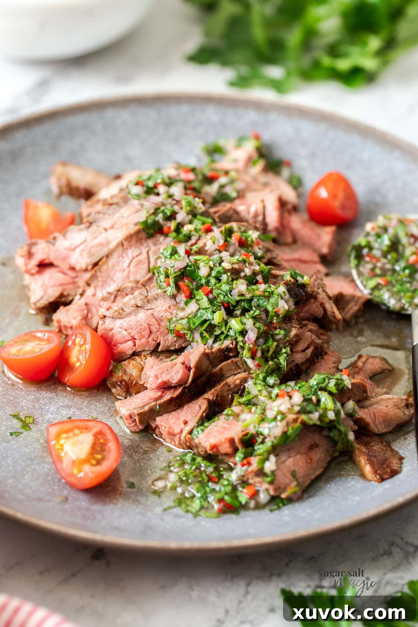 Sliced steak on a grey plate with green sauce over it.