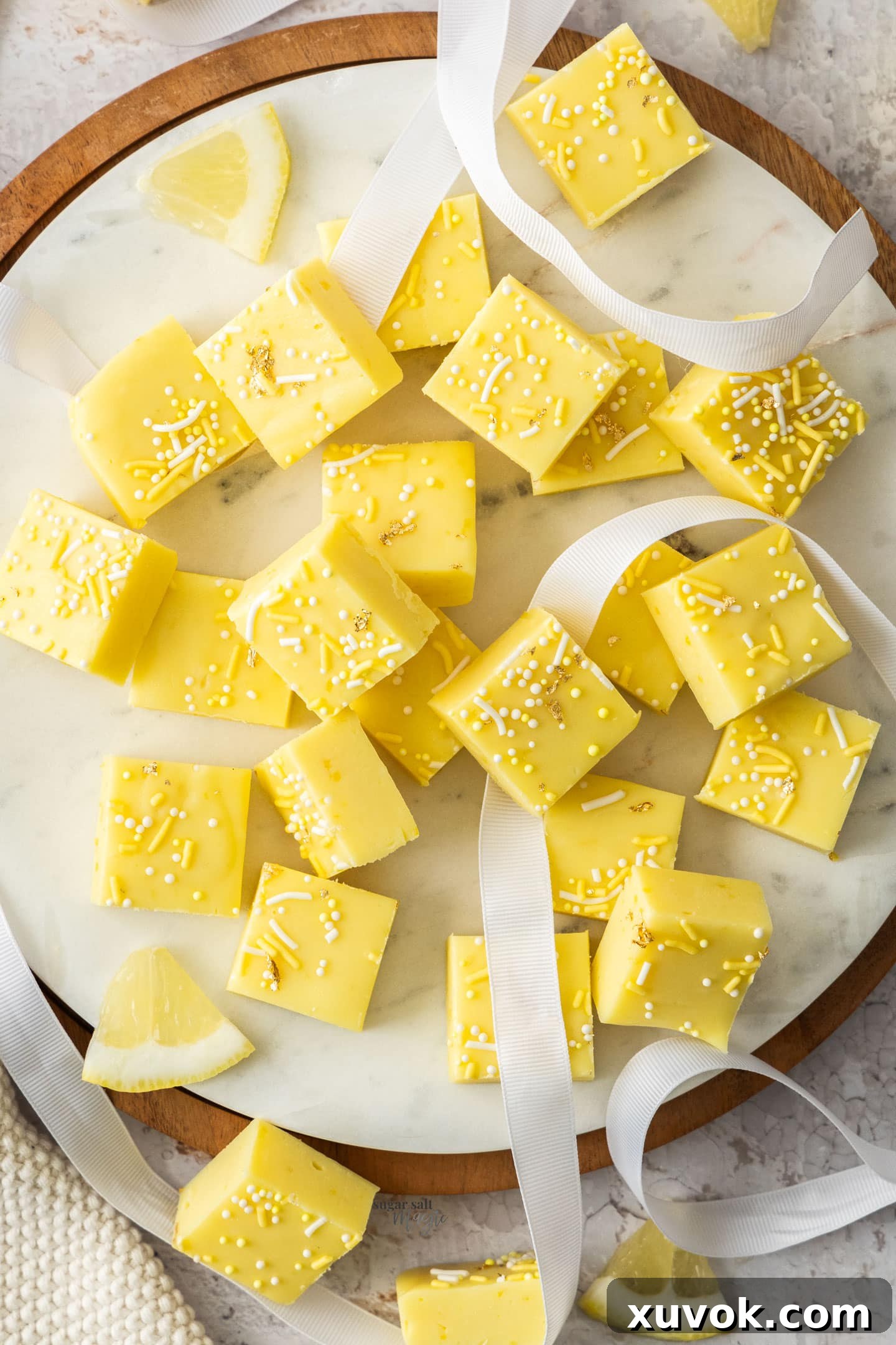 Top down view of a batch of bright yellow lemon fudge squares on a marble platter, garnished with a few sprinkles.